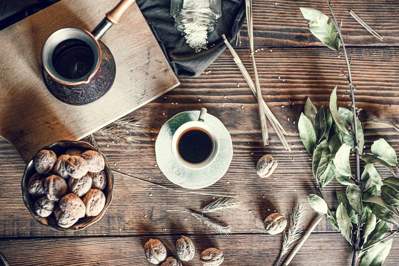 Coffee pot, a cup of filter coffee and a bowl of walnuts on a rustic wooden table