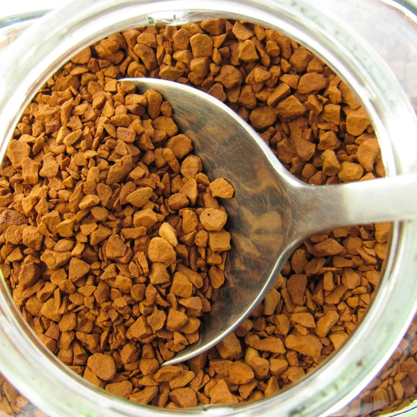 Instant coffee granules in a glass jar with a spoon