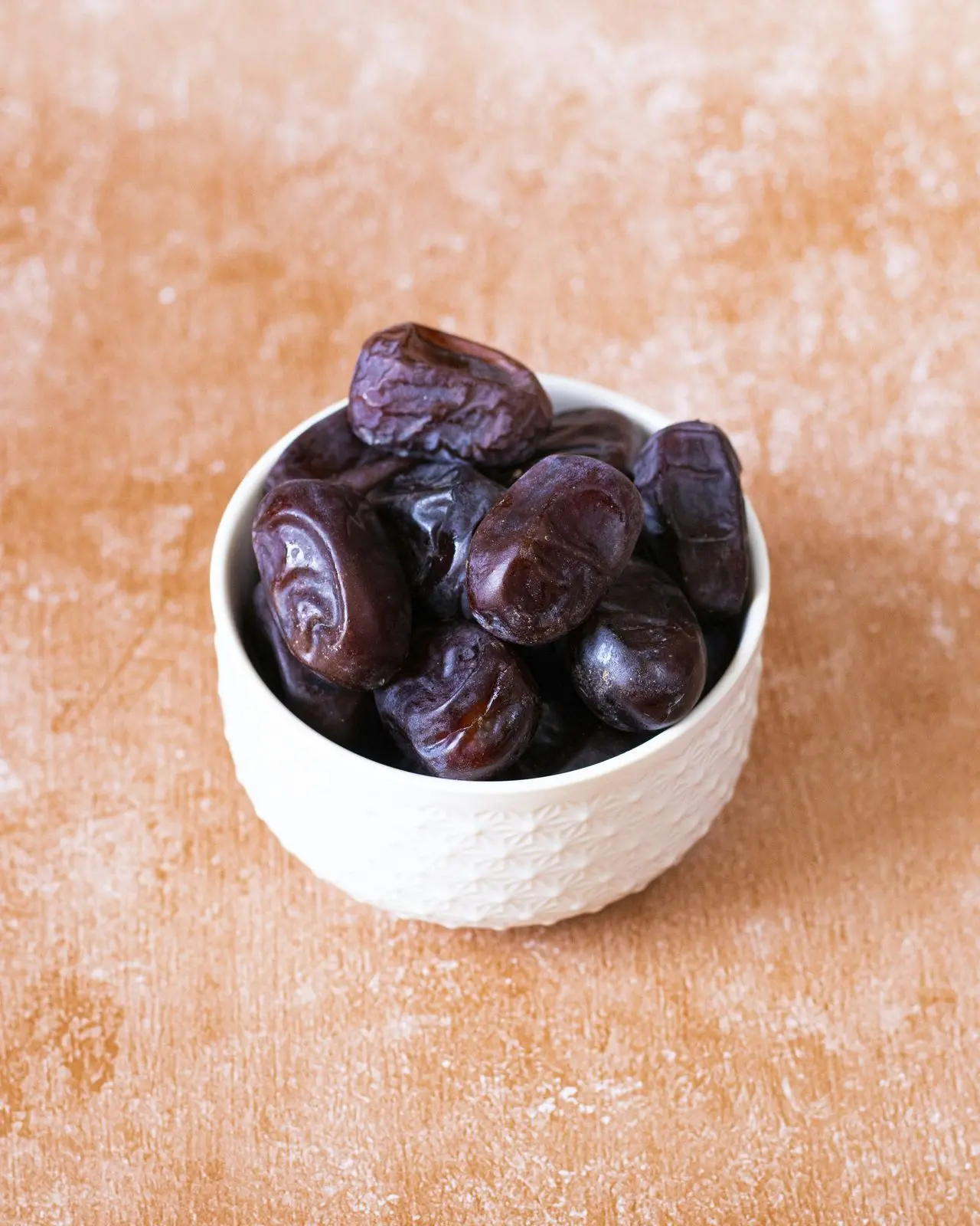 Soft dark Kimia dates in a white bowl